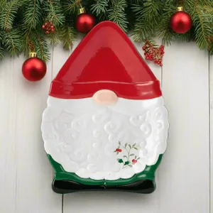 A festive gnome-shaped serving platter with a red hat, white beard featuring swirling patterns, and a small holly decoration, set against a wooden background with evergreen branches and red ornaments.