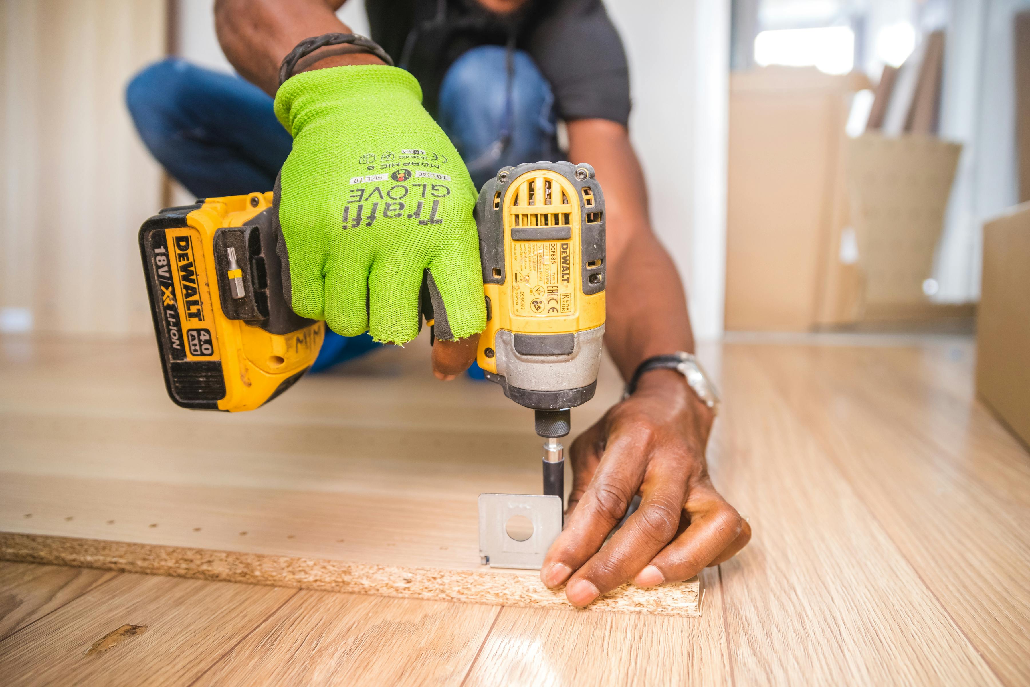 A person is using a yellow and black cordless drill to secure a bracket onto a wooden floor.