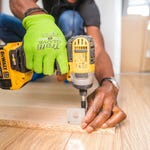 A person is using a yellow and black cordless drill to secure a bracket onto a wooden floor.