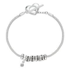 A silver bracelet features a heart-shaped clasp and three engraved beads with personalized names, alongside a charm with a small gemstone.