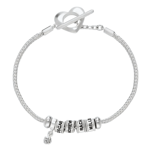 A silver bracelet features a heart-shaped clasp and three engraved beads with personalized names, alongside a charm with a small gemstone.