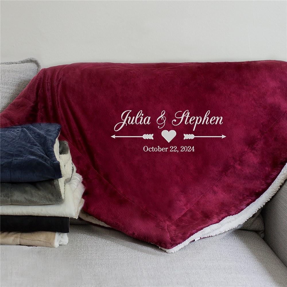 A plush burgundy throw blanket on a couch features the names \“Julia & Stephen\“ with a heart and arrow design, and the date \“October 22, 2024\“ embroidered on it.