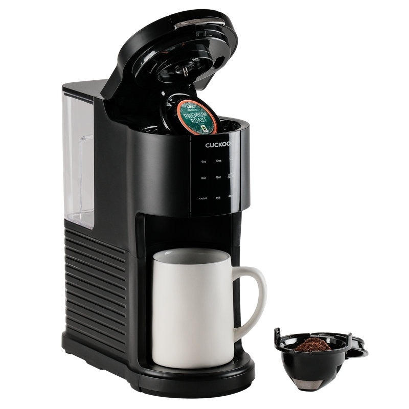 A Cuckoo coffee maker with an open lid to insert pods, a mug underneath, and a separate reusable coffee filter filled with grounds.