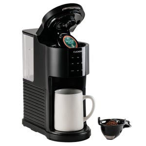 A Cuckoo coffee maker with an open lid to insert pods, a mug underneath, and a separate reusable coffee filter filled with grounds.
