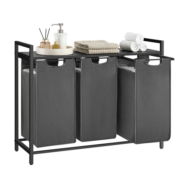 A sleek, black metal-frame laundry hamper with three gray fabric bags, featuring cut-out handles. The top surface holds folded towels and toiletries on a tray for added functionality.