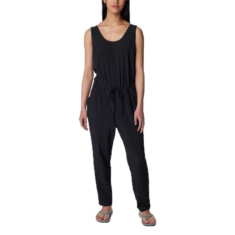 A woman is wearing a sleeveless black jumpsuit with a scoop neckline and a drawstring waist, paired with flip-flops.