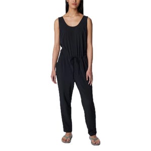 A woman is wearing a sleeveless black jumpsuit with a scoop neckline and a drawstring waist, paired with flip-flops.