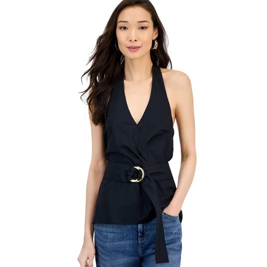 A woman wearing a black halter top with a V-neckline and a belt featuring a gold ring buckle, paired with blue jeans.