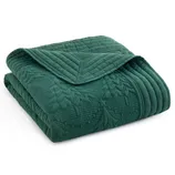 A folded dark green quilt with a quilted tree pattern design.