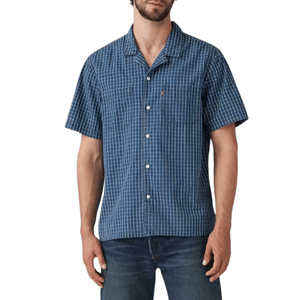 A man is wearing a short-sleeve blue checked button-up shirt paired with dark blue jeans.