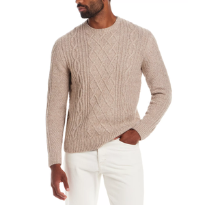 A beige cable-knit sweater paired with white pants, featuring a textured pattern and a round neckline.