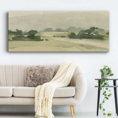 A panoramic canvas depicts a serene, monochromatic landscape with gentle hills and sparse trees, hanging above a sofa with a textured throw and a plant beside it.