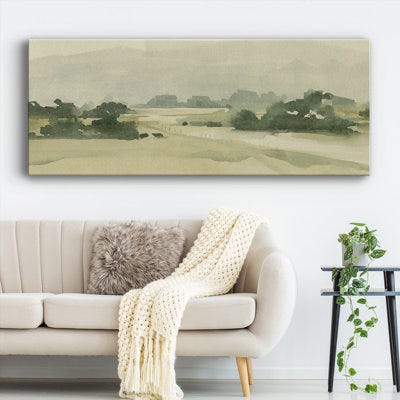A panoramic canvas depicts a serene, monochromatic landscape with gentle hills and sparse trees, hanging above a sofa with a textured throw and a plant beside it.