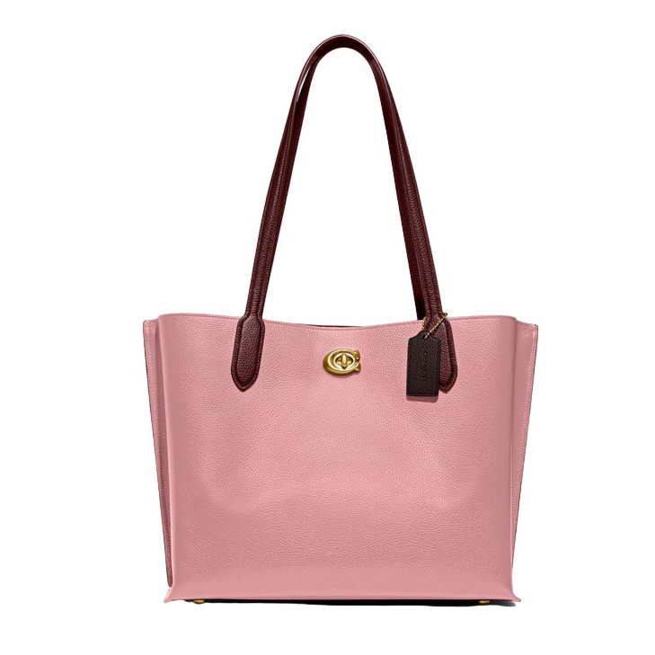 A pink tote bag with brown handles and a gold-tone logo, accompanied by a black tag.