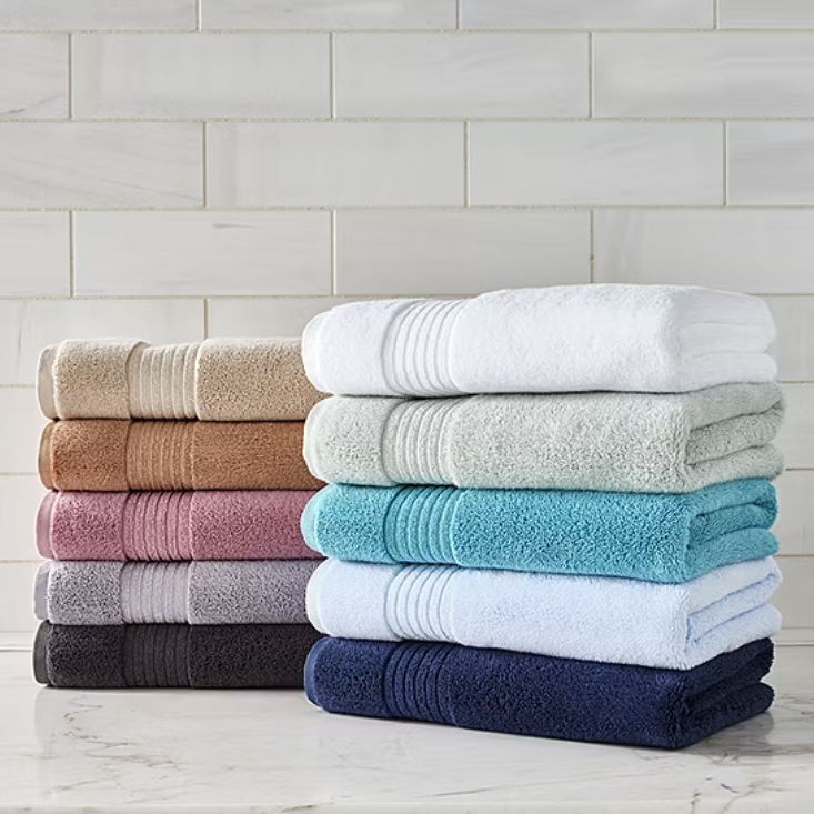 Liz Claiborne Plush Bath Towels, available in various colors like beige, pink, blue, and white, are neatly stacked. These towels feature a soft, textured design with horizontal ribbing accents.