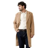 A man is wearing a tan overcoat, a white button-up shirt, dark blue jeans, and brown leather ankle boots.