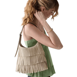 A woman is wearing a sleeveless green top and carrying a beige fringed shoulder bag. She has a ponytail and is wearing a bracelet.