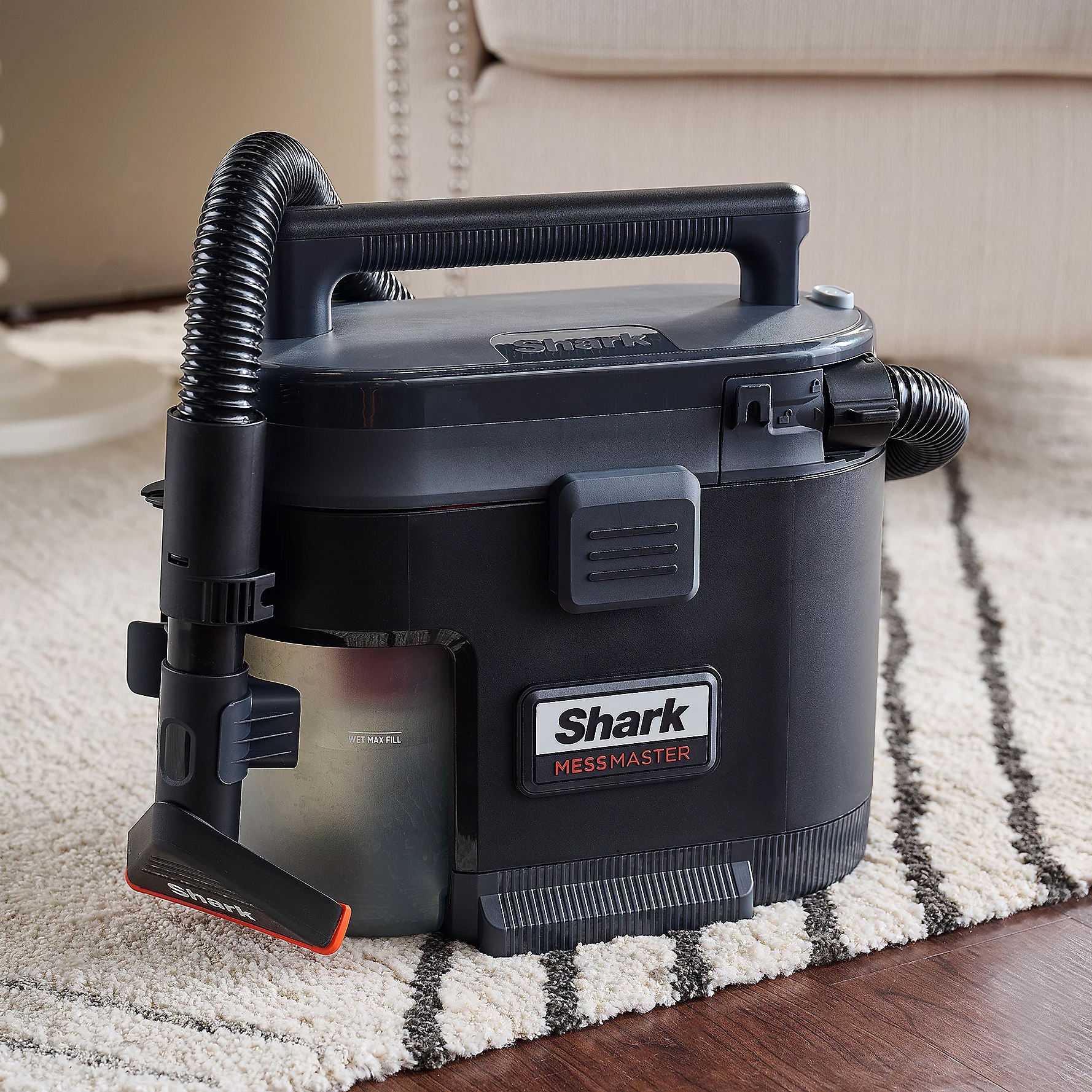 A black Shark MessMaster wet/dry vacuum cleaner with a flex hose and detachable crevice tool on a carpet.