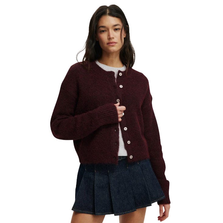 A woman is wearing a burgundy button-up cardigan over a white top paired with a pleated dark denim skirt.
