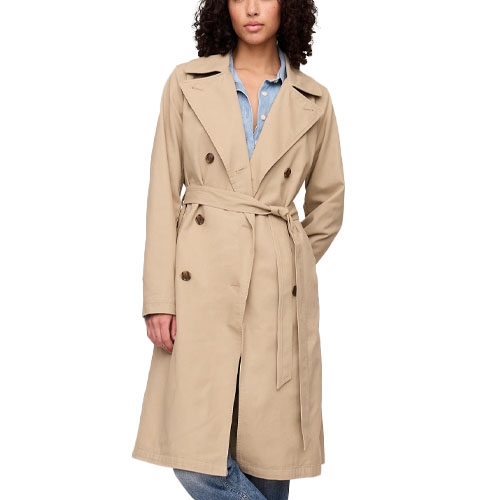 A woman wearing a beige double-breasted trench coat with a waist tie, layered over a denim shirt and jeans.