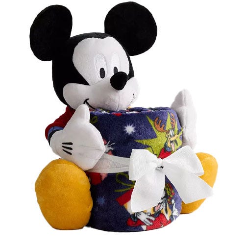 A plush toy resembling a classic cartoon character holds a patterned fleece blanket tied with a white ribbon, featuring festive designs.