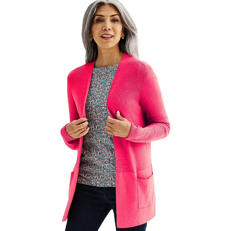 A woman wears a bright pink open-front cardigan over a floral-patterned shirt and dark jeans.