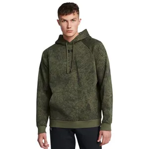 A man wears an olive green Under Armour hoodie with a subtle camouflage pattern and black pants.