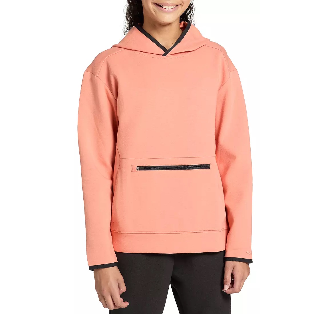 A person wearing a peach-colored hoodie with black trim and a zippered front pocket, paired with black pants.