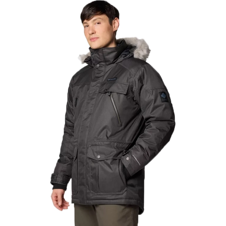 The Columbia Barlow Pass Down Jacket is a dark-colored, insulated parka with a fur-lined hood, several zippered and snap-button pockets, and a water-resistant finish designed for cold weather conditions.