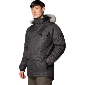 The Columbia Barlow Pass Down Jacket is a dark-colored, insulated parka with a fur-lined hood, several zippered and snap-button pockets, and a water-resistant finish designed for cold weather conditions.