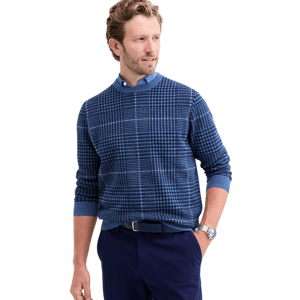 A man is wearing a blue, patterned sweater over a blue shirt paired with navy pants.