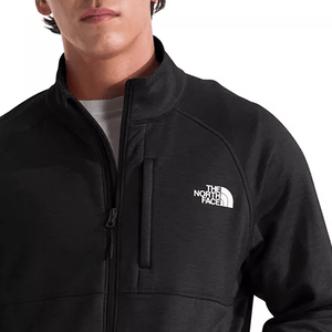 A person wearing a black, zip-up North Face jacket with a logo on the chest.