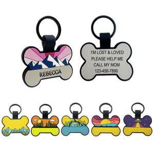 Bone-shaped pet ID tags with colorful designs; one tag displays the name \“Rebecca\“ and mountains, another has contact text and a phone number. Additional tags feature various scenic illustrations.