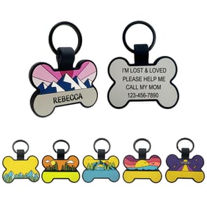 Bone-shaped pet ID tags with colorful designs; one tag displays the name \“Rebecca\“ and mountains, another has contact text and a phone number. Additional tags feature various scenic illustrations.