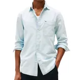 A person is wearing a light blue denim shirt with a chest pocket, rolled-up sleeves, and partially buttoned over a white undershirt, paired with dark pants.