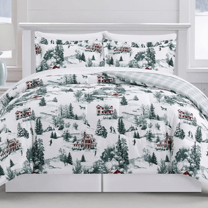 A winter-themed bedding set featuring a snowy village scene with red houses and evergreen trees. The comforter is reversible with a plaid pattern on the other side.