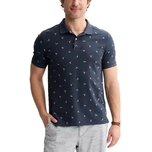A man is wearing a navy polo shirt with small, light pink and white flamingo prints and light gray shorts. He has his left hand in his pocket and is wearing a watch on his right wrist.