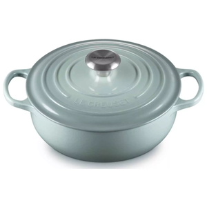A Le Creuset Dutch oven in a light blue color with a metal knob, featuring dual handles on each side and the brand name embossed on the lid.