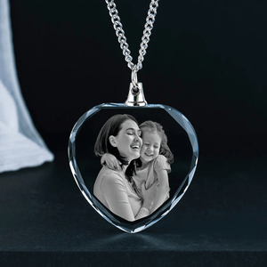 A heart-shaped crystal pendant necklace features a black-and-white photo of a woman and child embracing, with the image elegantly engraved inside the crystal.