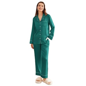 A person is wearing green satin pajamas with white trim and buttons, paired with fluffy white slippers.