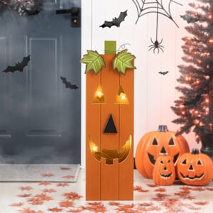 A decorative wooden pumpkin sign with lights, featuring a jack-o'-lantern face, surrounded by Halloween decorations including spider webs, bats, autumn leaves, and carved pumpkins.