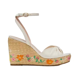Kate Spade Strawberry Sandals feature a white, knotted strap design with an ankle buckle. The wedge heel is made of a woven material with colorful floral and strawberry embroidery.
