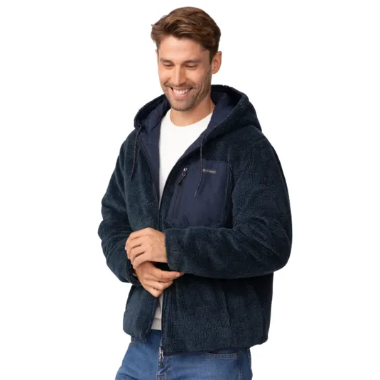 A man is wearing a dark blue sherpa jacket with a hood and a front zippered pocket, paired with a white shirt and blue jeans.