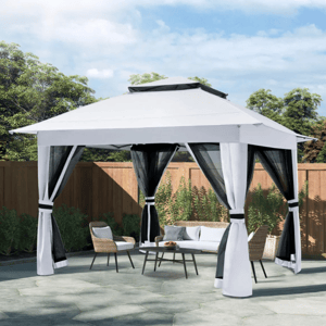 A white outdoor gazebo with black mesh curtains is set up on a paved area, accompanied by wicker chairs and a coffee table, surrounded by a wooden fence and greenery.
