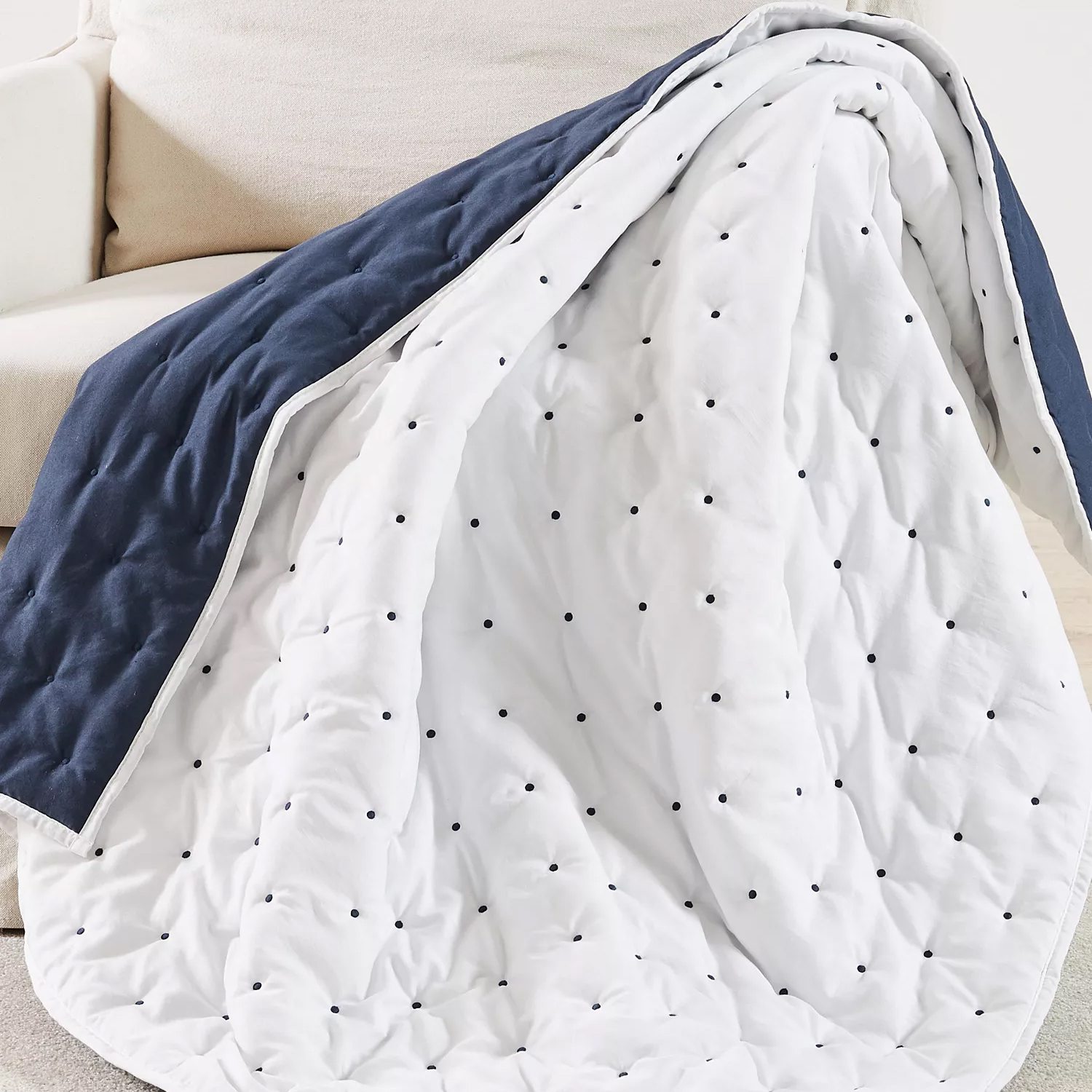 A quilt draped over a sofa, featuring a reversible design with a navy blue side and a white side with black polka dots.