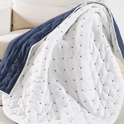 A quilt draped over a sofa, featuring a reversible design with a navy blue side and a white side with black polka dots.