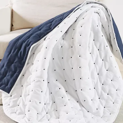 A quilt draped over a sofa, featuring a reversible design with a navy blue side and a white side with black polka dots.