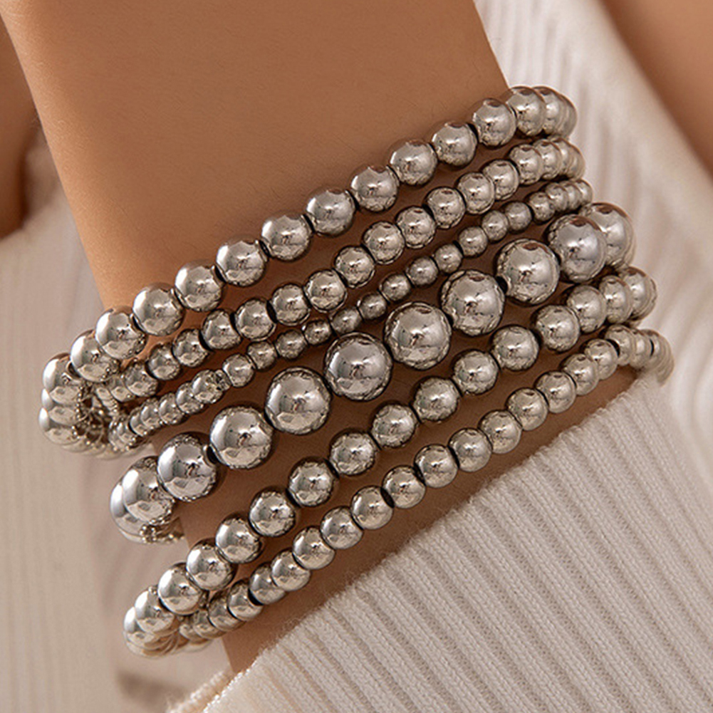 A multi-strand bracelet with shiny silver beads in varying sizes, wrapped elegantly around a wrist against a white ribbed fabric background.