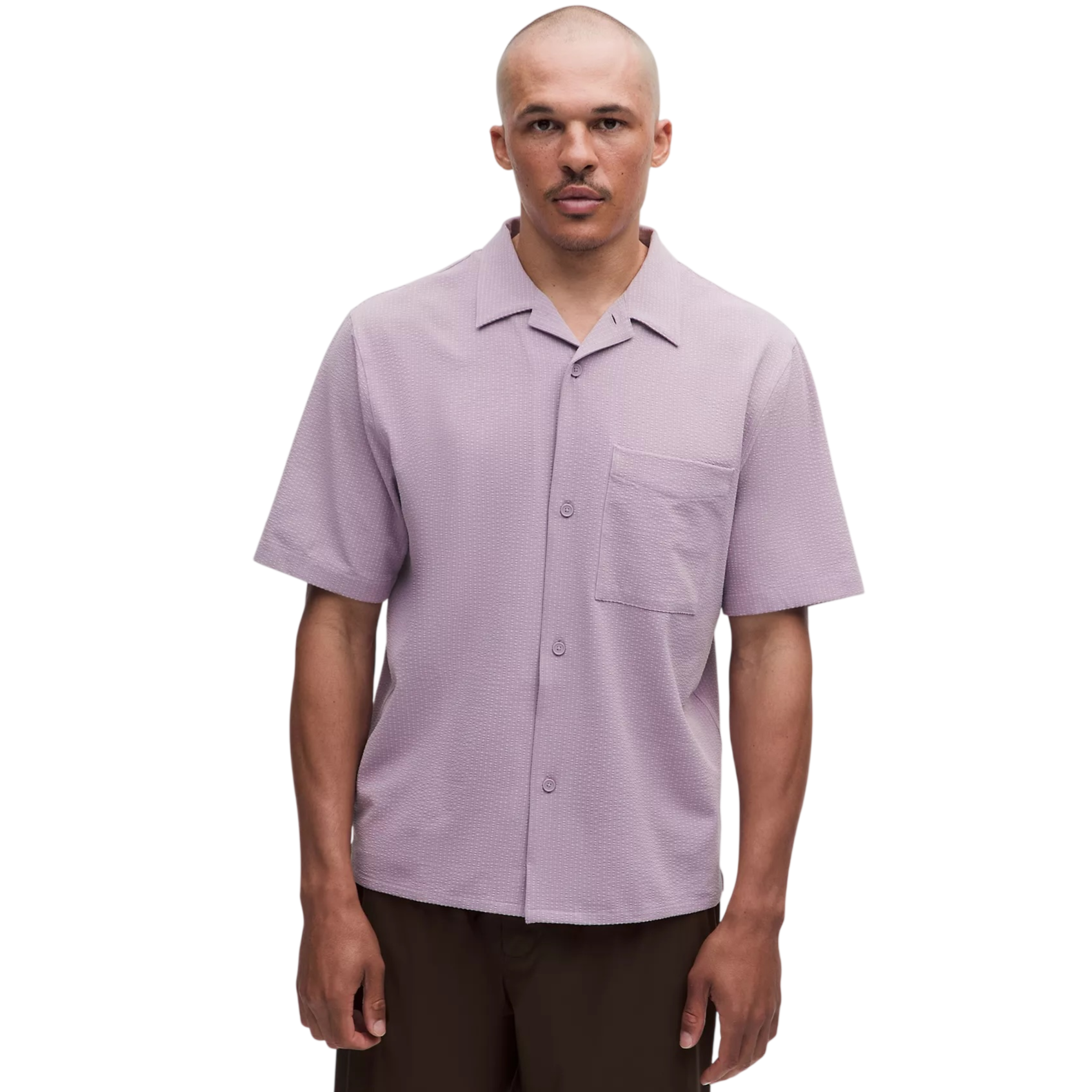 A man wears a light purple short-sleeve button-up shirt with a pocket on the chest. He pairs it with dark brown pants.