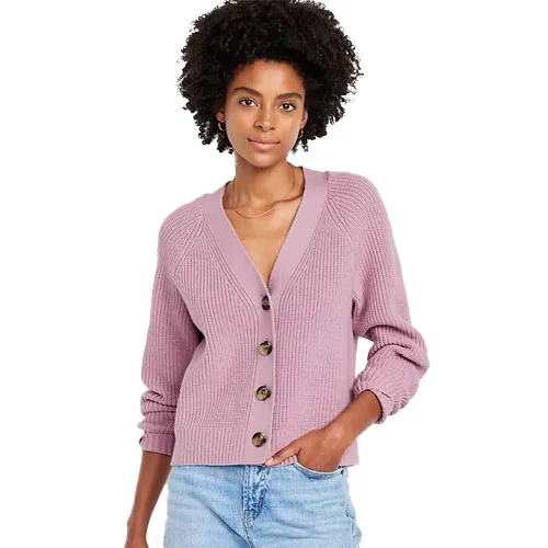 A woman is wearing a ribbed pink cardigan with three dark buttons and light blue jeans.